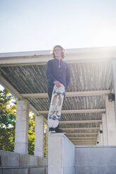 Portrait of young male urban skateboarder standing on wall with skateboard - CUF14851