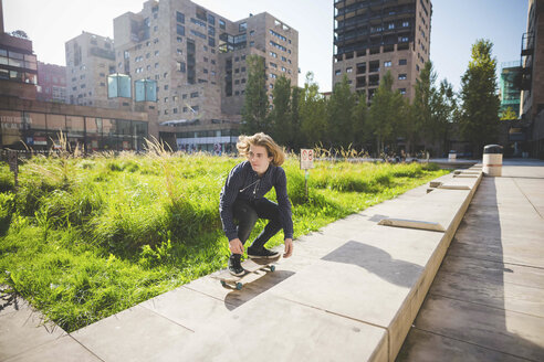 Junger männlicher Skateboarder hockt beim Skateboardfahren auf einer städtischen Mauer - CUF14856