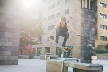 Junger männlicher Skateboarder, der über den Sitz einer städtischen Halle springt - CUF14858