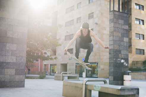 Junger männlicher Skateboarder, der über den Sitz einer städtischen Halle springt - CUF14858