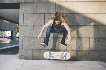 Young male urban skateboarder doing skateboarding jump trick above skateboard - CUF14872