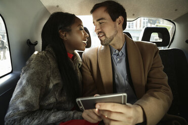 Couple sitting in back of taxi, face to face, smiling - CUF14881