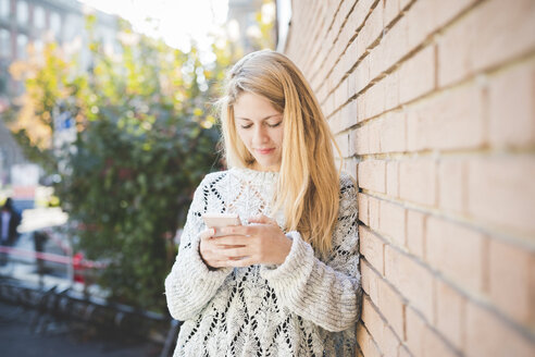 Frau, die eine SMS auf ihrem Smartphone schreibt, gegen eine Backsteinmauer - CUF14990