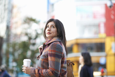 Mature female tourist with takeaway coffee on city street, Tokyo, Japan - CUF15024