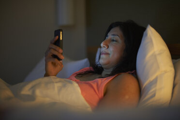 Reife Frau liest nachts im Hotelbett Smartphone-Texte - CUF15025