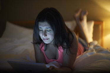Reife Frau, die nachts auf dem Hotelbett liegend ein digitales Tablet benutzt - CUF15026