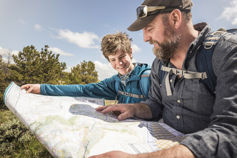 Hiking father and teenage son sitting reading folding map, Cody, Wyoming, USA stock photo