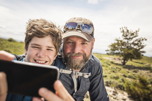 Nahaufnahme eines Vaters und eines Sohnes im Teenageralter, die beim Wandern ein Smartphone-Selfie machen, Cody, Wyoming, USA - CUF15055