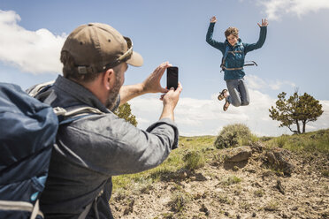 Father photographing teenage son jumping mid air on hiking trip, Cody, Wyoming, USA - CUF15058