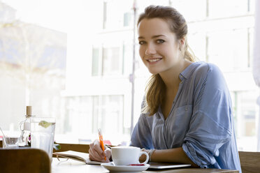 Young woman in cafe writing, looking at camera smiling - CUF15095