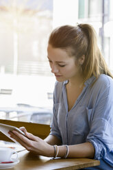 Young woman in cafe looking down using digital tablet - CUF15096