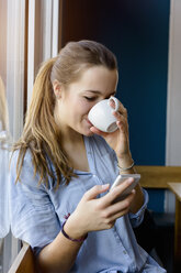 Junge Frau hält Smartphone und trinkt Kaffee - CUF15097