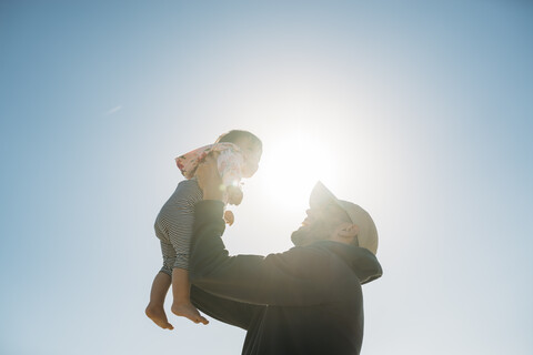 Vater hält kleines Mädchen im Gegenlicht hoch, lizenzfreies Stockfoto