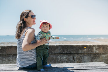 Frankreich, zufriedene Mutter und kleines Mädchen auf einer Bank an der Strandpromenade - GEMF02042