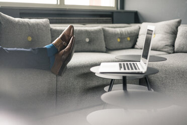 Businessman's feet on couch next to laptop - JOSF02191