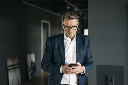 Mature businessman standing in office using cell phone - JOSF02202