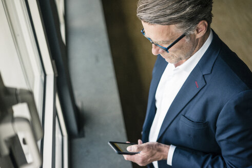 Reifer Geschäftsmann steht am Fenster und benutzt ein Mobiltelefon - JOSF02211