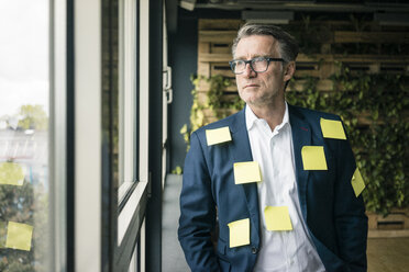 Serious mature businessman covered with sticky notes looking out of window - JOSF02220