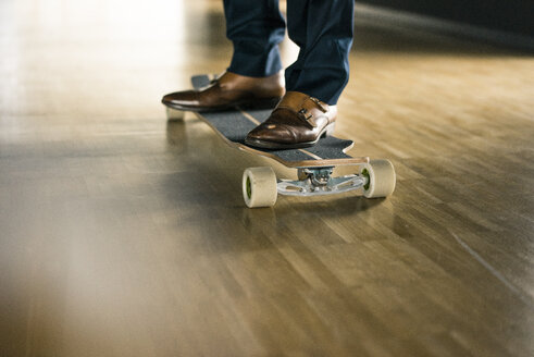 Businessman riding longboard on wooden floor - JOSF02231