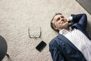 Reifer Geschäftsmann auf Teppich liegend neben Mobiltelefon - JOSF02236