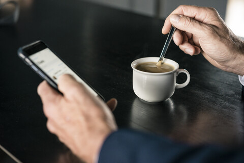 Nahaufnahme eines Geschäftsmannes mit einer Tasse Kaffee und einem Mobiltelefon, lizenzfreies Stockfoto