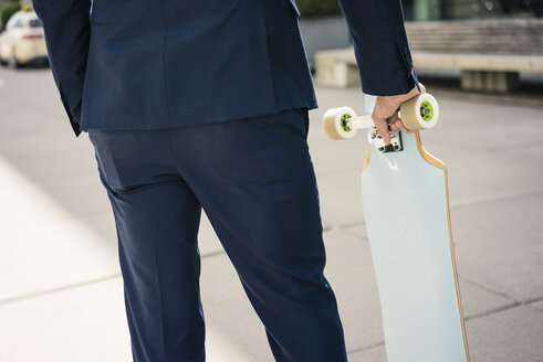 Businessman holding longboard outdoors - JOSF02246