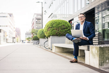 Mature businessman using laptop on bench outdoors - JOSF02248