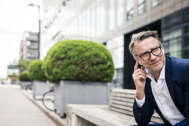 Smiling mature businessman sitting on bench outdoors wearing earbuds - JOSF02250