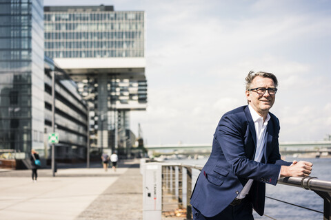 Lächelnder reifer Geschäftsmann, der eine Pause am Flussufer einlegt, lizenzfreies Stockfoto