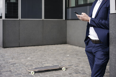 Businessman with longboardusing cell phone outdoors - JOSF02257
