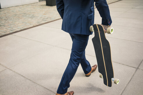 Geschäftsmann zu Fuß mit Longboard im Freien - JOSF02259