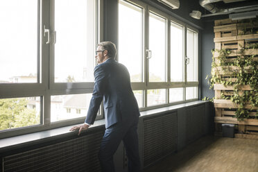 Reifer Geschäftsmann steht am Fenster im Büro - JOSF02269