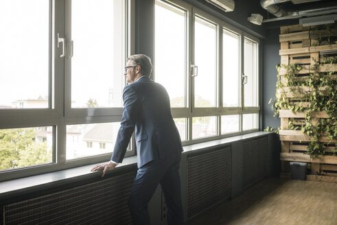 Reifer Geschäftsmann steht am Fenster im Büro - JOSF02269