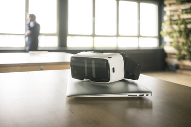 VR-Brille und Laptop auf dem Tisch im Büro mit Geschäftsmann im Hintergrund - JOSF02271