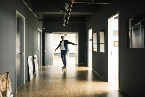 Geschäftsmann fährt Longboard auf dem Büroboden - JOSF02274