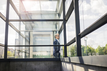 Mature businessman at glass structure in the city looking around - JOSF02285