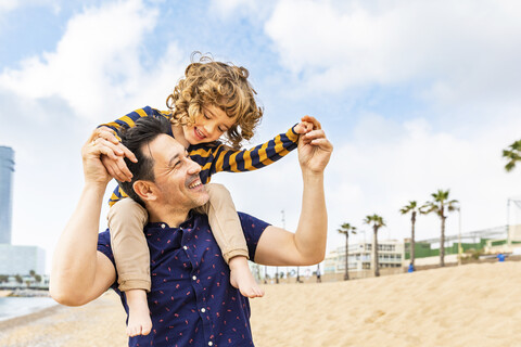 Spanien, Barcelona, Vater mit Sohn am Strand beim Huckepackfahren, lizenzfreies Stockfoto