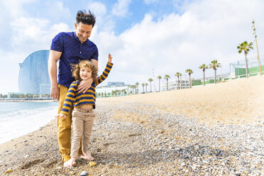 Spanien, Barcelona, kleiner Junge mit Füßen über seinem Vater am Strand mit Kieselsteinen - WPEF00364