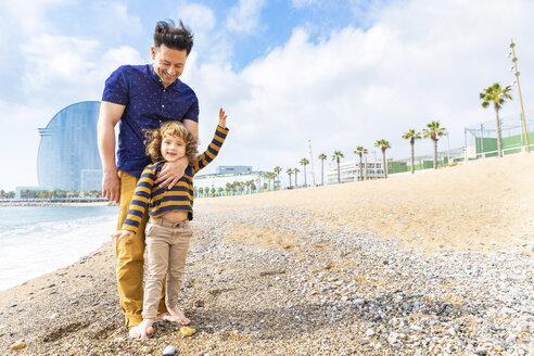 Spain, Barcelona, young boy with feet over his father on beach with pebbles - WPEF00364