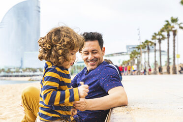 Spain, Barcelona, young boy playing with sand, his father sitting next to him and smiling - WPEF00368