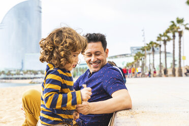Spanien, Barcelona, kleiner Junge spielt mit Sand, sein Vater sitzt neben ihm und lächelt - WPEF00368