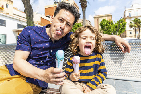 Spain, Barcelona, happy father and son sitting on bench enjoying an ice cream - WPEF00380