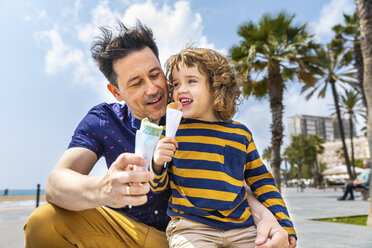 Spanien, Barcelona, Vater und Sohn genießen ein Eis am Meer - WPEF00381