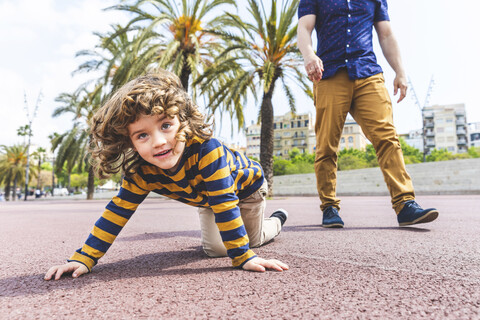 Spain, Barcelona, young boy crawling next to his father on seaside promenade stock photo