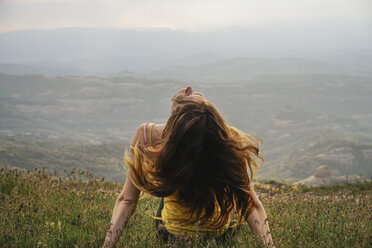 Spain, Barcelona, back view of young woman sitting on meadow tossing her hair - AFVF00544