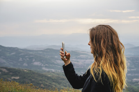 Spanien, Barcelona, junge Frau macht Selfie mit Smartphone auf dem Berg Montcau, lizenzfreies Stockfoto