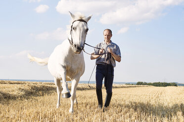 Mann trainiert trabendes weißes Pferd auf einem Feld - CUF15135