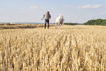 Mann trainiert galoppierendes weißes Pferd auf einem Feld - CUF15137