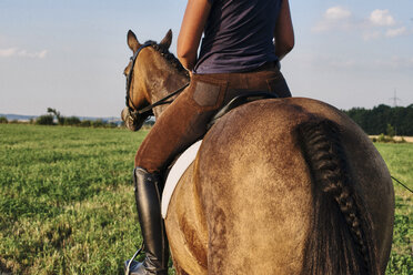 Rückansicht einer Frau, die ein braunes Pferd auf einem Feld reitet - CUF15139
