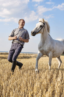 Männlicher Trainer läuft vor einem weißen Pferd auf einem Feld - CUF15142